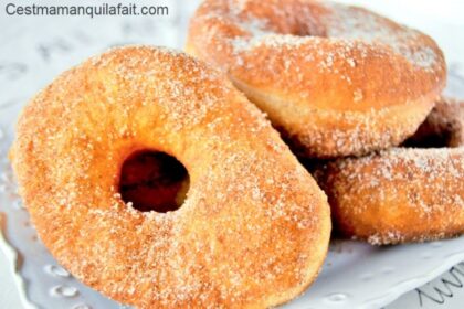 Beignets maison en forme d’anneaux, croustillants et dorés, recouverts de sucre et présentés sur un plateau.