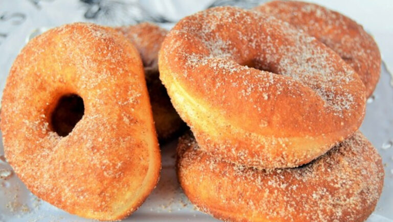 La recette secrète des beignets en pâte à pizza : plus légers que des donuts, prêts en minutes, impossible d’y résister ! Beignets dorés réalisés avec de la pâte à pizza, saupoudrés de sucre et disposés en pile sur une assiette.